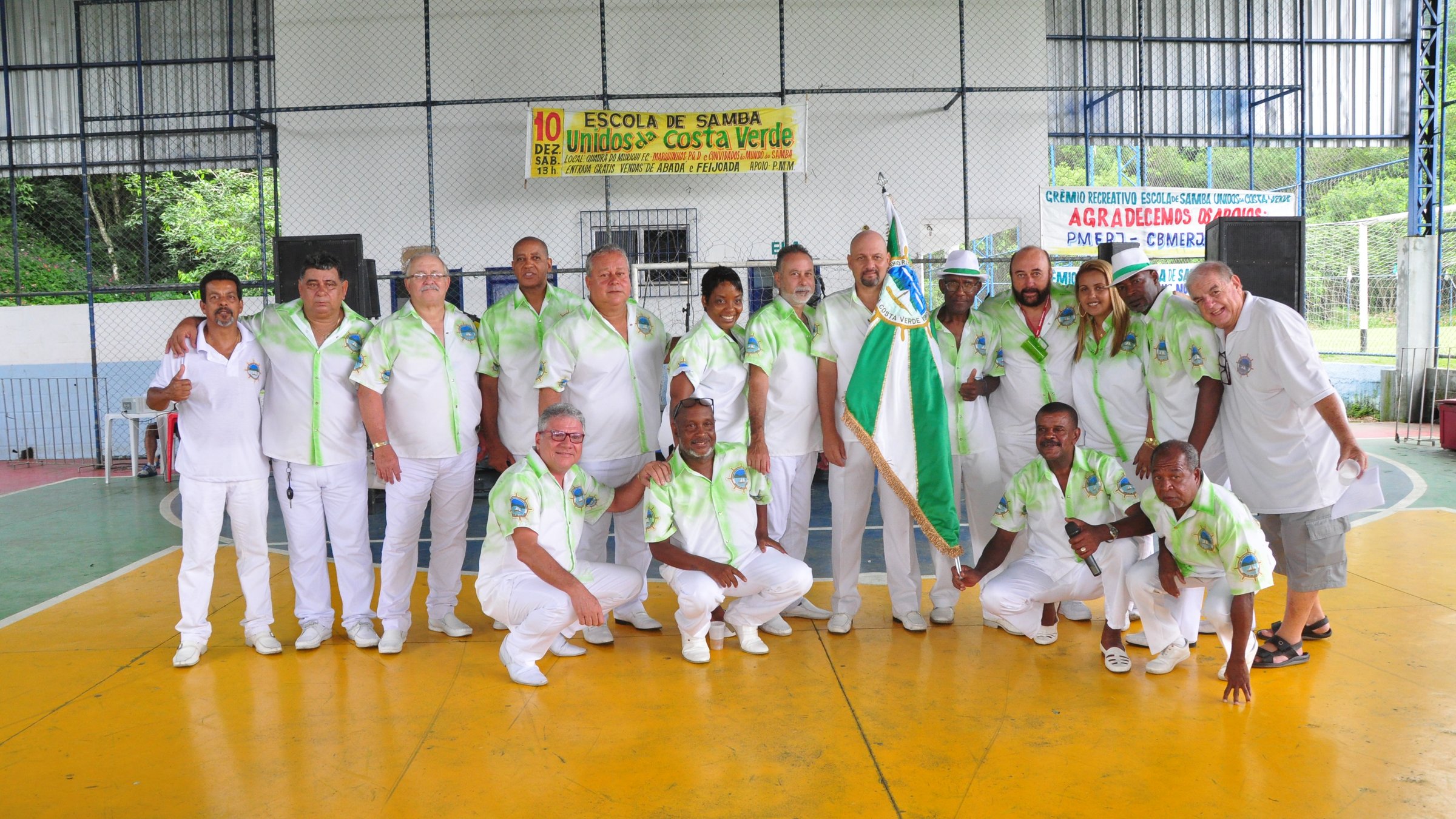 Diretoria da GRESUCV Unidos da Costa Verde reunida com a bandeira da escola na quadra do Muriqui F.C.